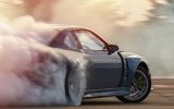 A silver two-door sports coupe burning rubber on an outdoor course with smoke drifting up behind it.