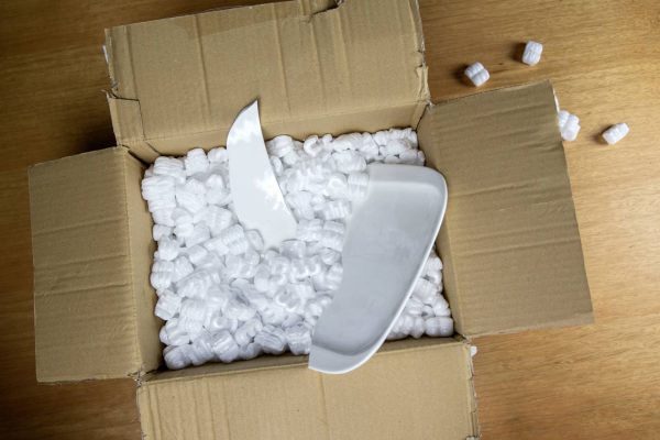 A brown cardboard box filled with Styrofoam packaging peanuts and two pieces of a broken plate inside.