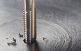 A threaded drill bit drilling into a piece of metal during thread milling. Burrs are sitting off to the side.