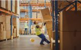 A warehouse worker totters backward, about to fall, as a stack of boxes tips forward toward them.