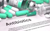 A sheet of paper with the word "Antibiotics" written on it, surrounded by capsule pills, tablets, and a needle.