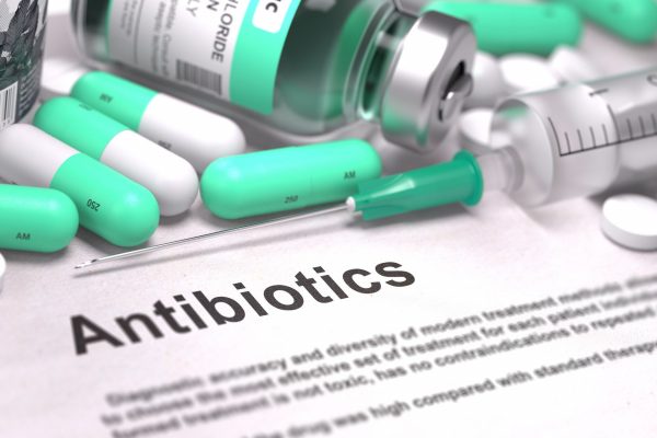A sheet of paper with the word "Antibiotics" written on it, surrounded by capsule pills, tablets, and a needle.
