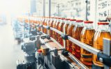 A large conveyor belt moves glass bottles filled with a brown liquid and red cap to a new location.