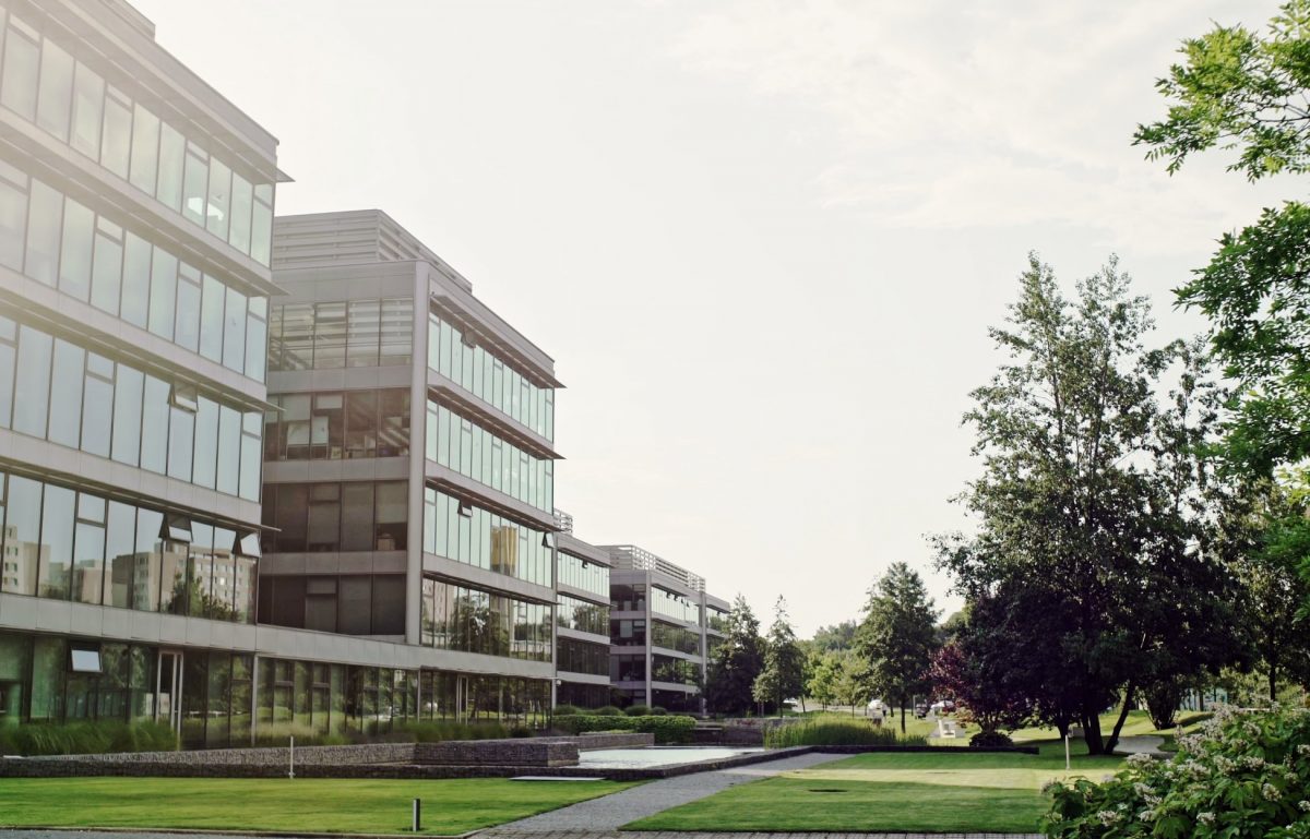 A large commercial building with an all-glass window exterior. The grass is freshly cut and the trees are in full bloom.