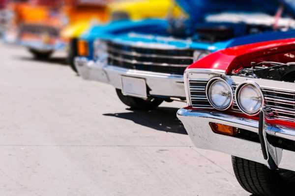 A lineup of classic cars of many different colors. The cars all have their hoods open.